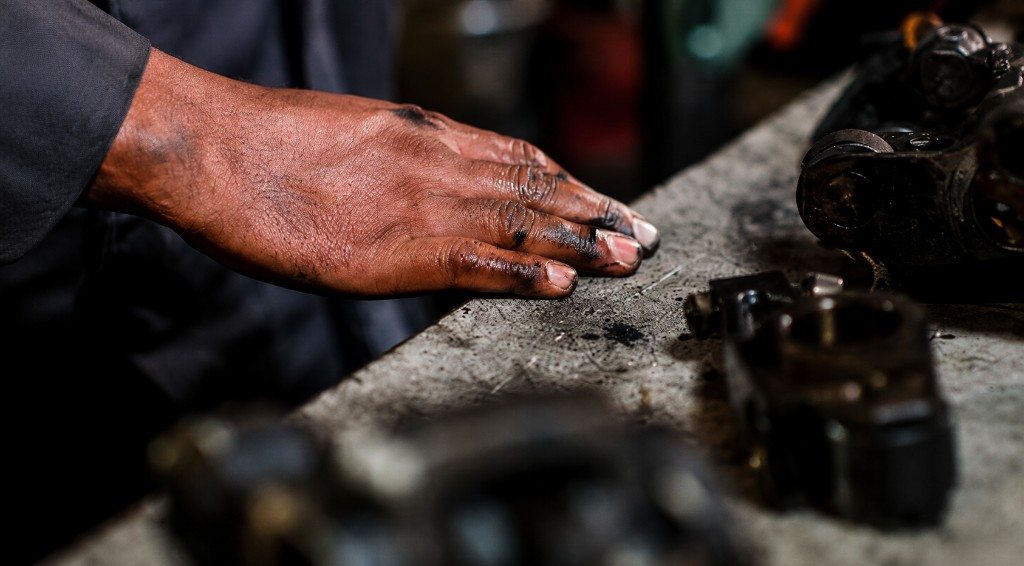 Mechanic's grease-covered hand on the workbench beside engine parts